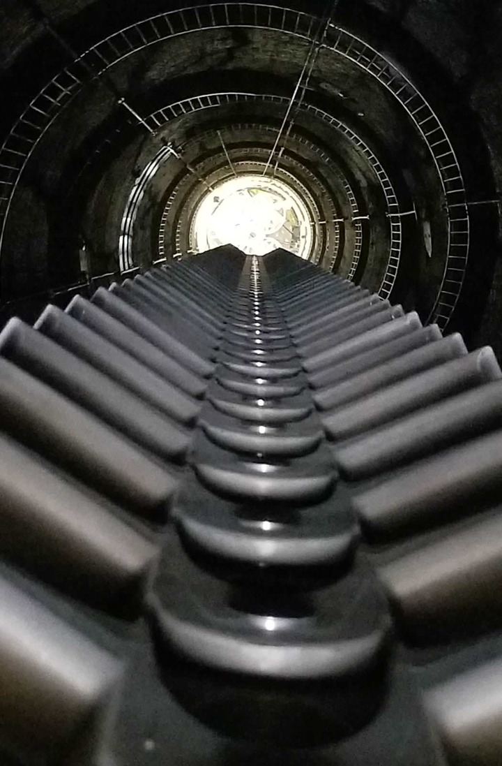 Vista desde la parte superior del pozo, mostrando la escalera en el borde y las ruedas dentadas en el centro.
